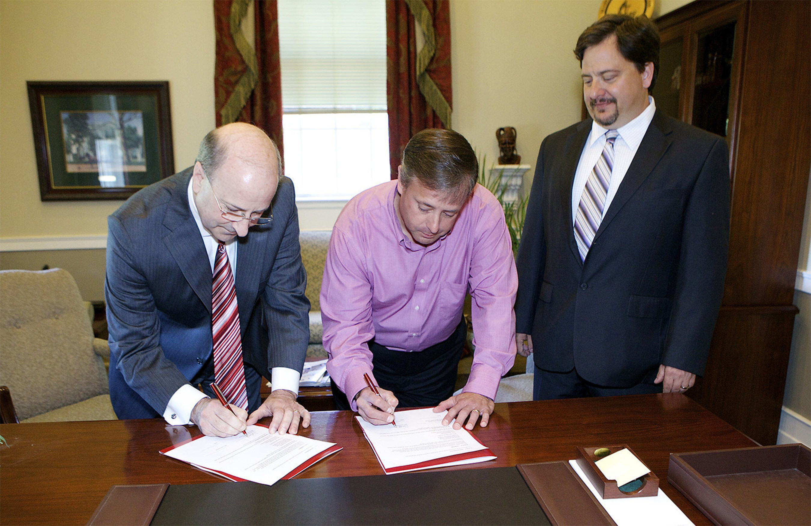 Troy Baxter (center), human resources director for NPC International's east division, and Martin Methodist College President Ted Brown sign the partnership agreement for MMC to offer online business degree opportunities to the company's employees. Dr. William Sodeman, chairman of the college's Johnston School of Business, looks on.