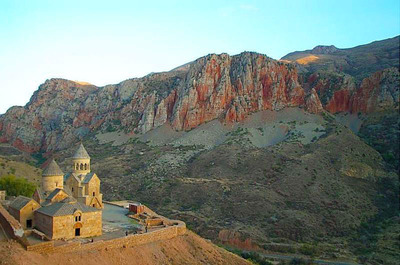Visit Armenia. Noravank monastery is a 13th century monastery, located 122 km from Yerevan in a narrow gorge made by the Darichay river, nearby the city of Yeghegnadzor, Armenia. The gorge is known for its tall, sheer, brick-red cliffs, directly across from the monastery. The monastery is best known for its two-storey S. Astvatsatsin church, which grants access to the second floor by way of narrow stones jutting out from the face of building.