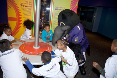 Visiting 1st graders and Poe of the Baltimore Ravens have fun generating power in the newly opened Power Up! exhibit at the Maryland Science Center.