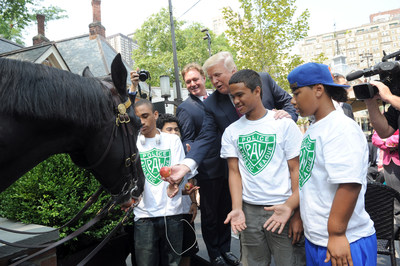 Donald Trump and Mark Bellissimo, CEO of Equestrian Sport Productions and owner and publisher of Chronicle of the Horse, joined by youth from the Police Athletic League NYC, feed an apple to NYPD Mounted Unit horse Torch, after announcing that the first ever "Central Park Horse Show Presented by Rolex" will come to Central Park's Trump Rink from September 18- 21, 2014 during a press conference at Tavern on The Green, Tuesday, July 29, 2014, in New York. (Photo by Diane Bondareff)