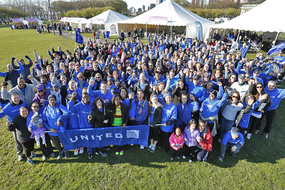 United employees gathered in grassy field, cheering and waving at camera, while holding a big United blue banner.