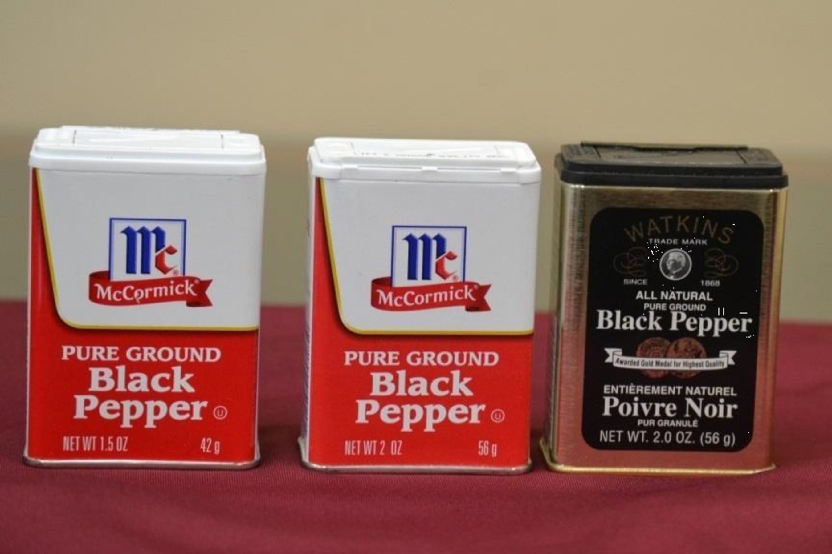 Photo showing traditional McCormick Small Tins with 1.5-ounce slack-fill and with traditional 2-ounce fill along with Watkins tin with 2-ounce fill.