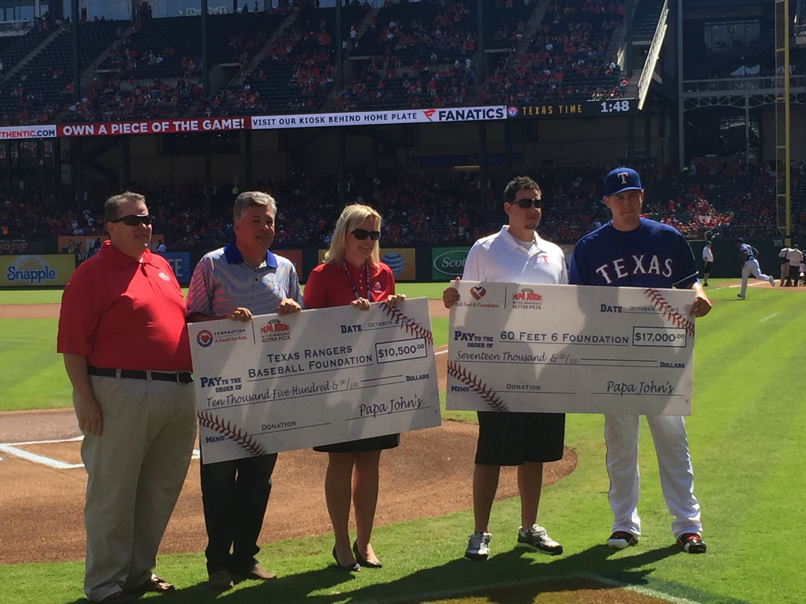Steve McNeil, operations vice president at Papa John's presents checks to the Texas Rangers Baseball Foundation and 60 Feet 6 at the game on October 4.