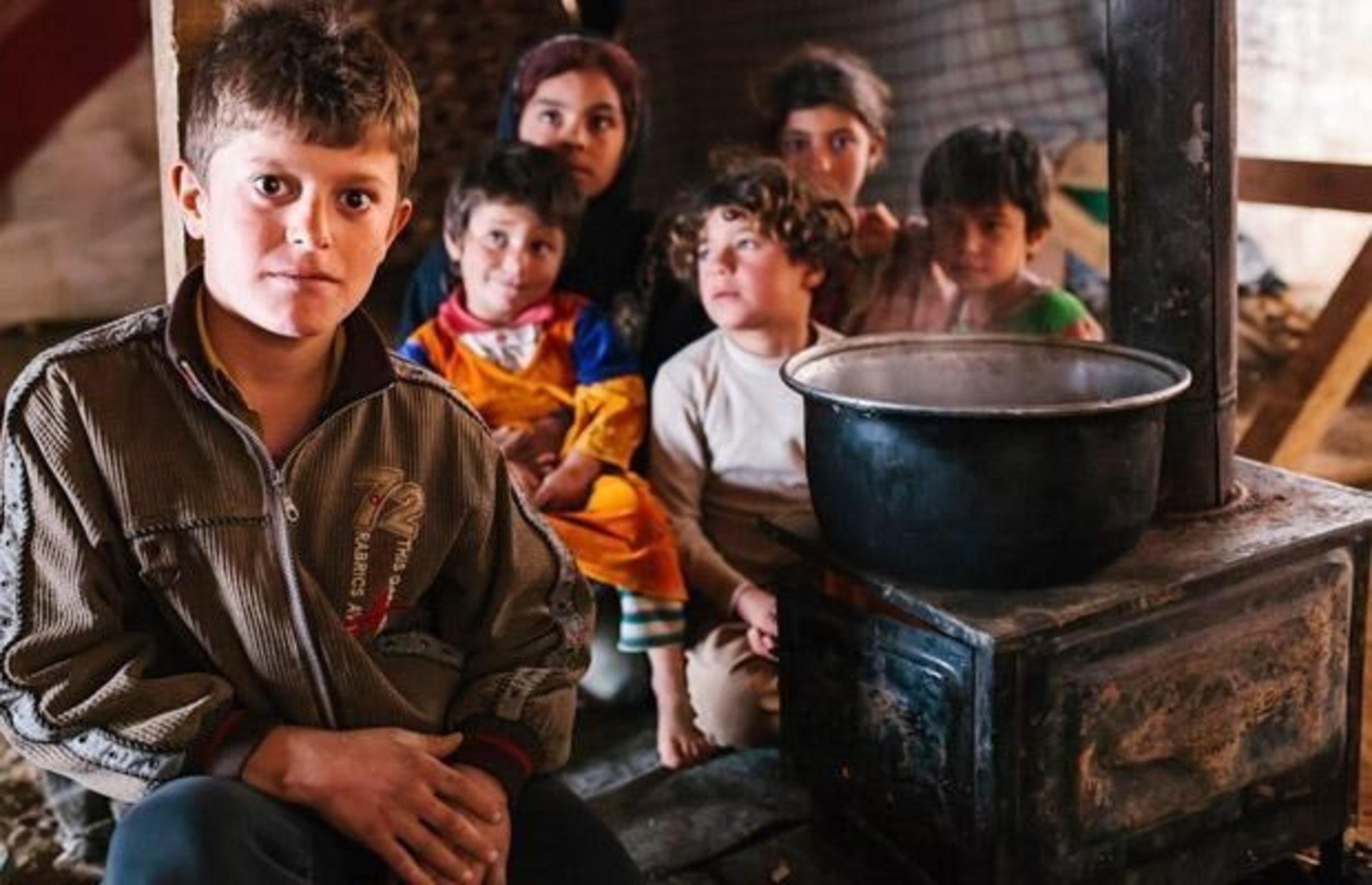 Syria refugees Adel and his siblings try to keep warm by the fire inside their makeshift home in the Bekaa Valley, Lebanon. ((c)2015 World Vision)