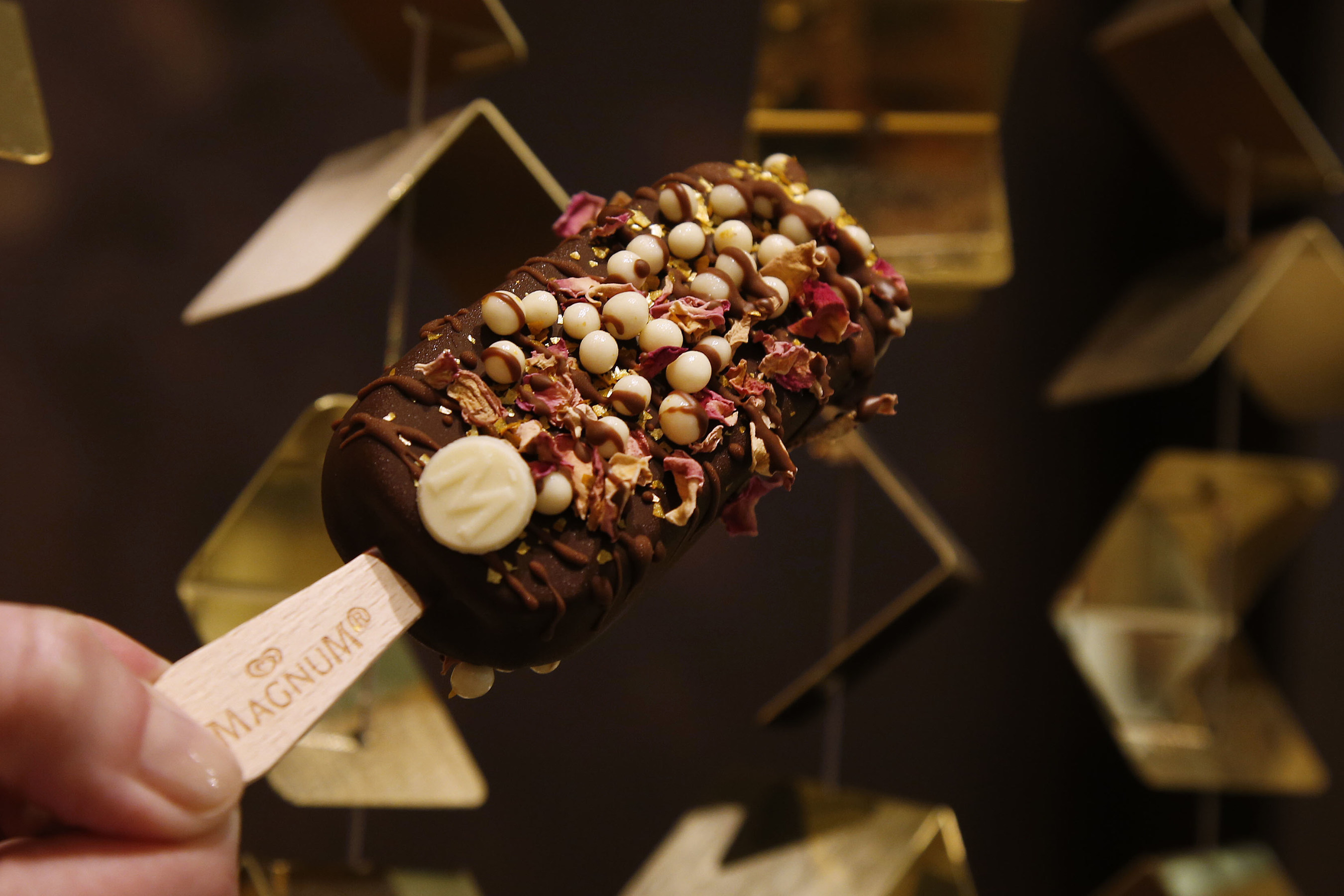 A close up of a custom MAGNUM ice cream bar at MAGNUM New York featuring vanilla bean ice cream hand-dipped in dark Belgian chocolate and topped with rose petals, gold flakes and white chocolate crispearls. This is the first U.S. storefront for MAGNUM Ice Cream; for more information, visit Facebook.com/MAGNUM. (Photo by Jason DeCrow for MAGNUM)
