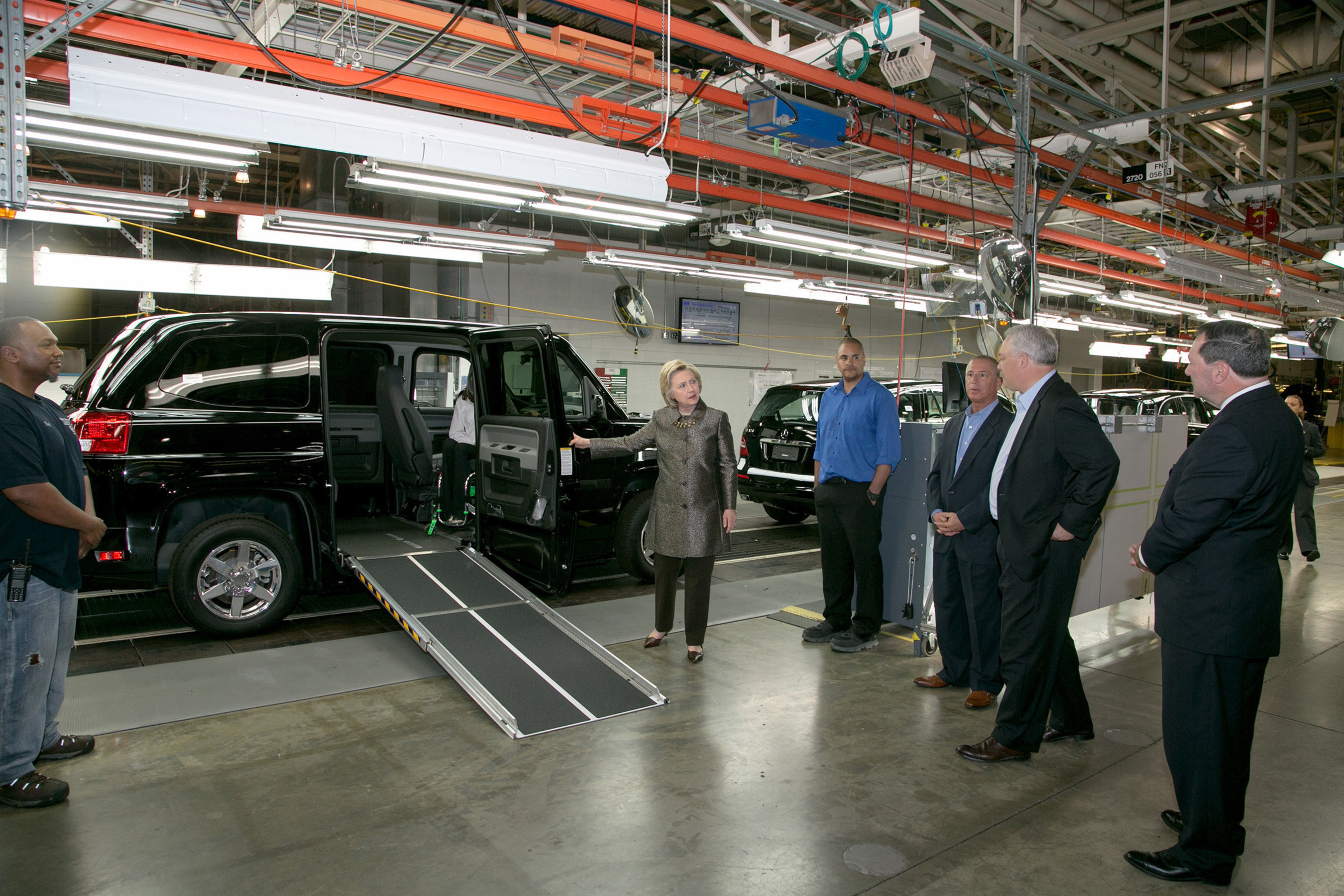Right to left - (Indiana Sen. Joe Donnelly AM General President and CEO, Andy Hove, AM General, Commercial President, Howard Glaser and Mrs. Clinton.)Upon seeing a demonstration of the MV-1 vehicle by Mobility Ventures employee, and former Ms. Wheelchair America, Erika Bogan, Mrs. Clinton commented later to a gathered crowd, "I want to thank you for coming up with the MV-1. What a remarkable invention, providing dignity, mobility to people with disabilities. I am thrilled that I got to see that."