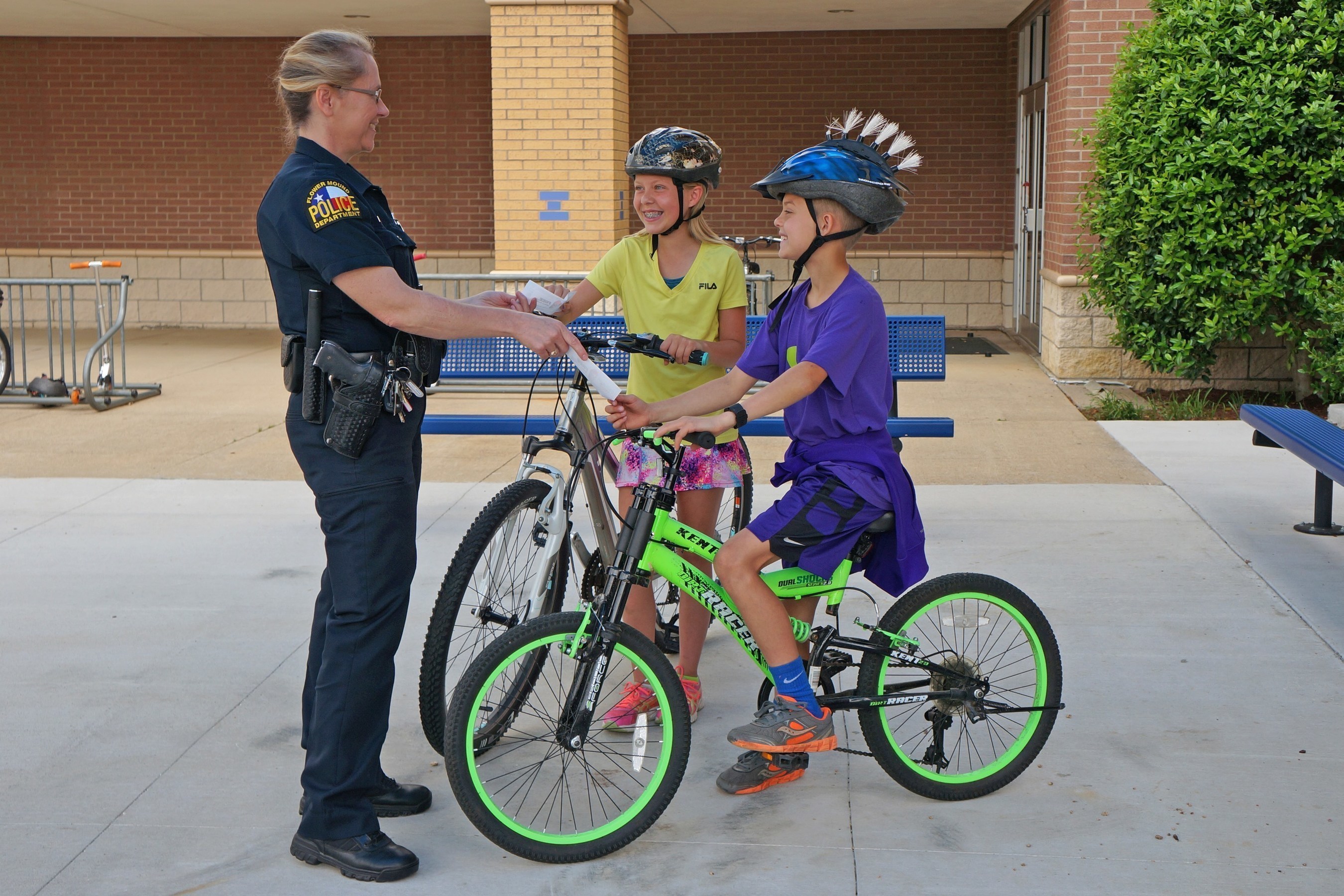 A police officer "tickets" kids with a 7-Eleven Operation Chill coupon for being safe by wearing helmets while riding their bikes.