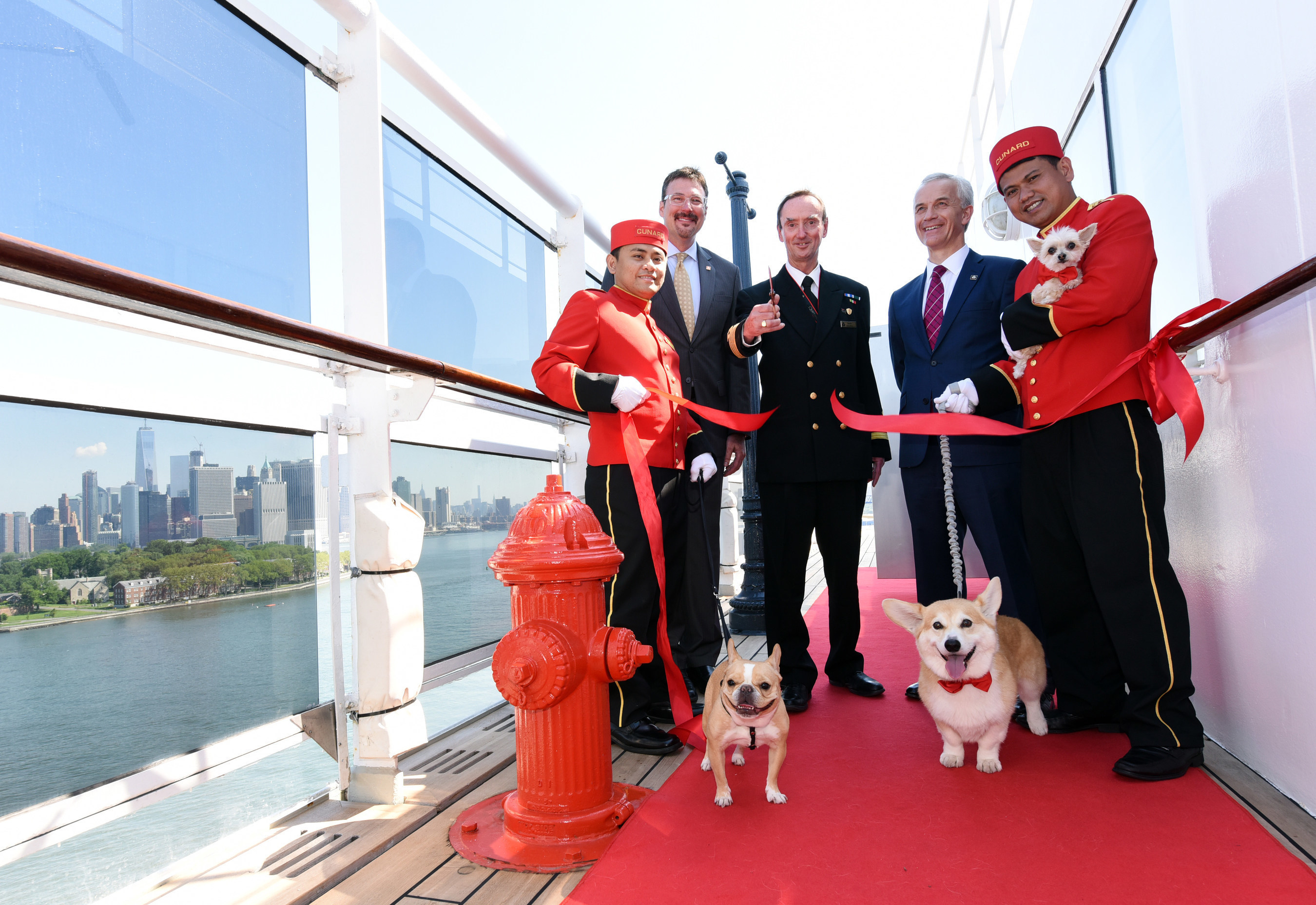 Richard Meadows, center left, President, Cunard, North America, Captain Christopher Wells, center, and David Noyes, center right, CEO, Cunard, joined by Cunard Kennel Masters, cut a ribbon to unveil the remastered kennels on the Queen Mary 2, the only passenger liner to carry pets. (Diane Bondareff/AP Images for Cunard)