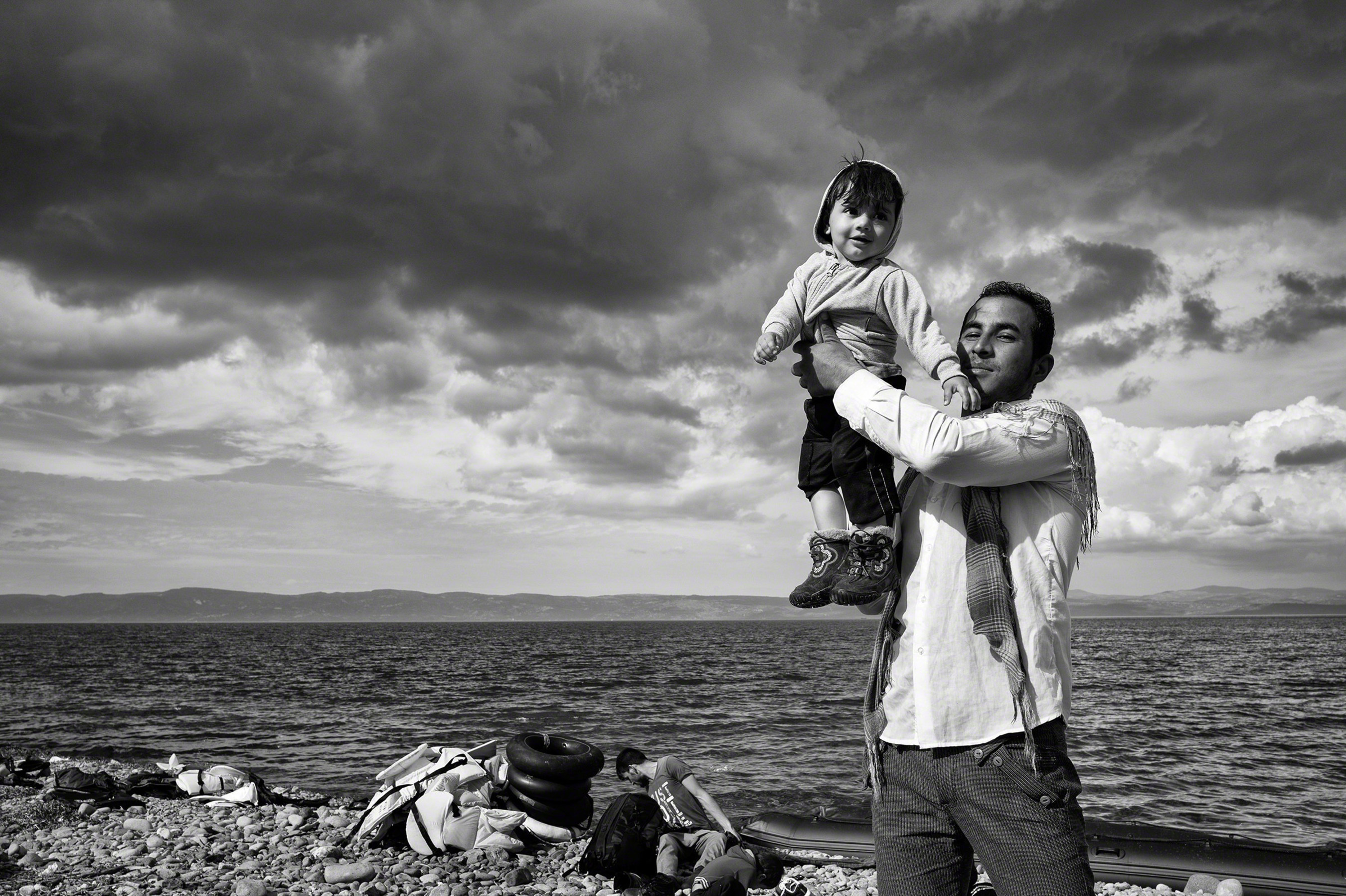 A father celebrates his family's safe passage to Lesbos after a stormy crossing over the Aegean Sea from Turkey. "REFUGEE," a groundbreaking exhibit that illuminates the plight of refugees through powerful and evocative photographs will open at the Newseum on Nov. 18. (C)Tom Stoddart