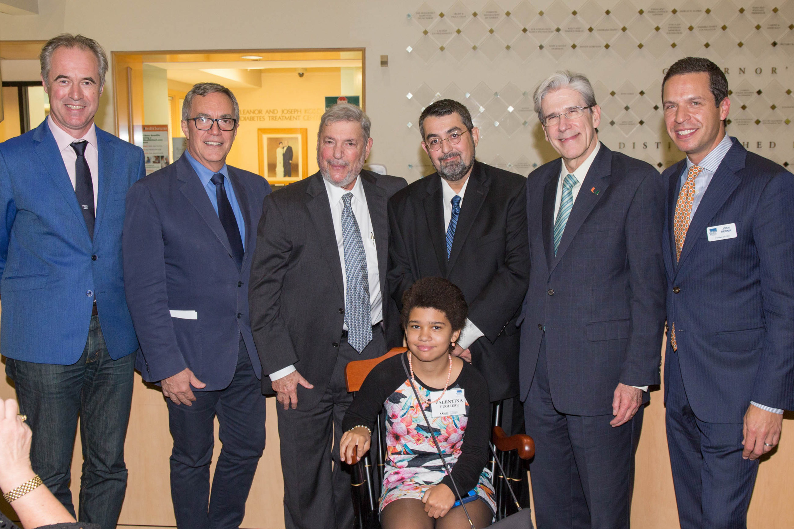 At the ceremony for the presentation of the J. Enloe and Eugenia J. Dodson Chair in Diabetes Research, speakers, including Bart Roep, M.D., Ph.D., Camillo Ricordi, M.D., Laurence B. Gardner, M.D., MACP, Alberto Pugliese, M.D., President Julio Frenk, and Joshua Rednik, pause for a photo, while Valentina Pugliese tries out her father's chair.