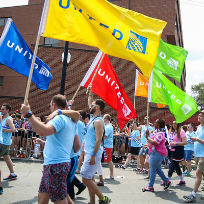People walking in a parade outside, waving brightly colored United flags.