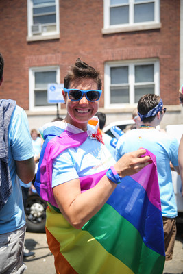 Smiling woman wearing sunglasses with a rainbow flag wrapped around her.