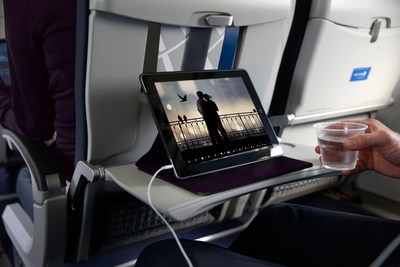 Seated passenger watching programming on tablet, with drink in hand