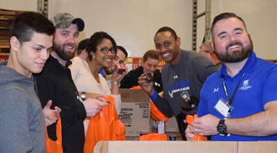 A group of injured service members and their families pack lunch bags at a food bank.