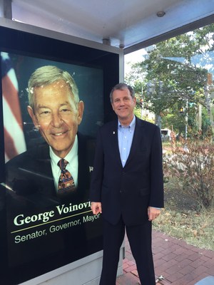 Sen. Sherrod Brown (D-Ohio) poses in front of one of the many digital signs that have dotted Washington D.C. bus shelters today commemorating the life of the late Senator George Voinovich.